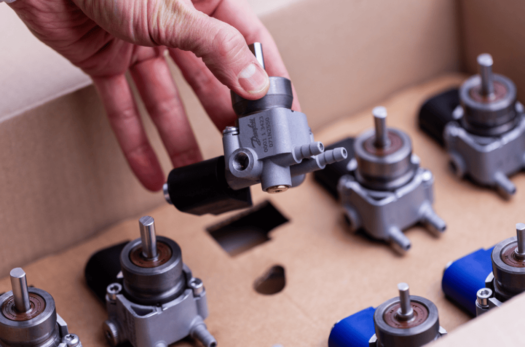 En hand lyfter en Danfoss oljepump ur en kartong med flera pumpar.